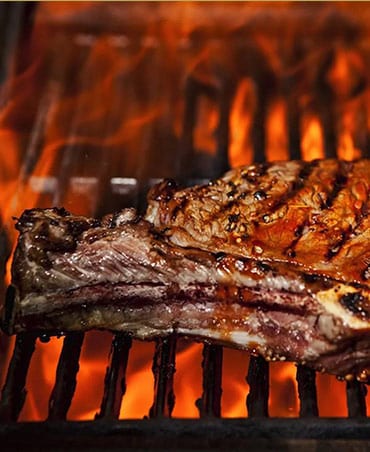 A steak is cooking on the grill with flames.